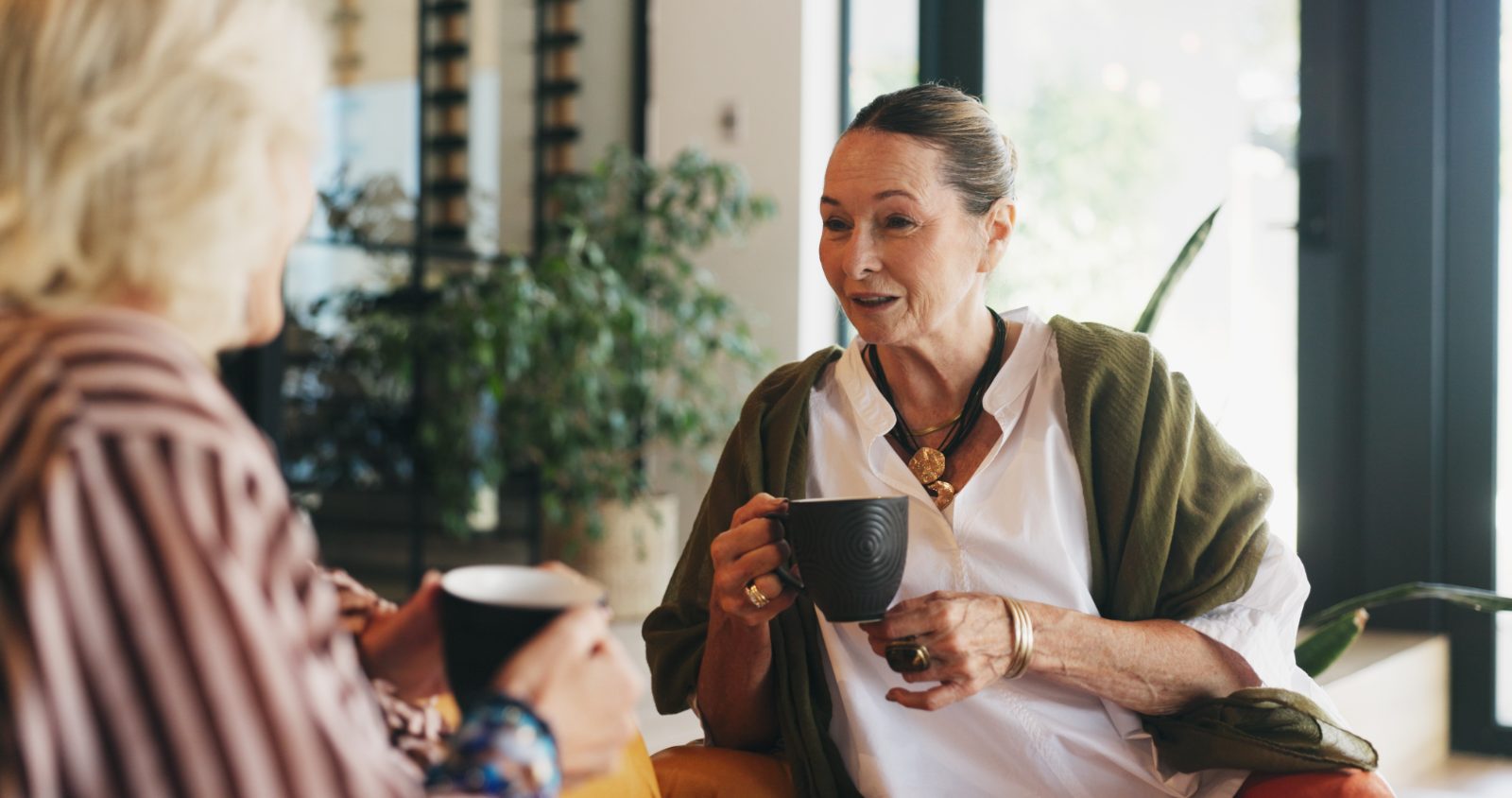 To damer drikker kaffe og prater sammen i en lys stue